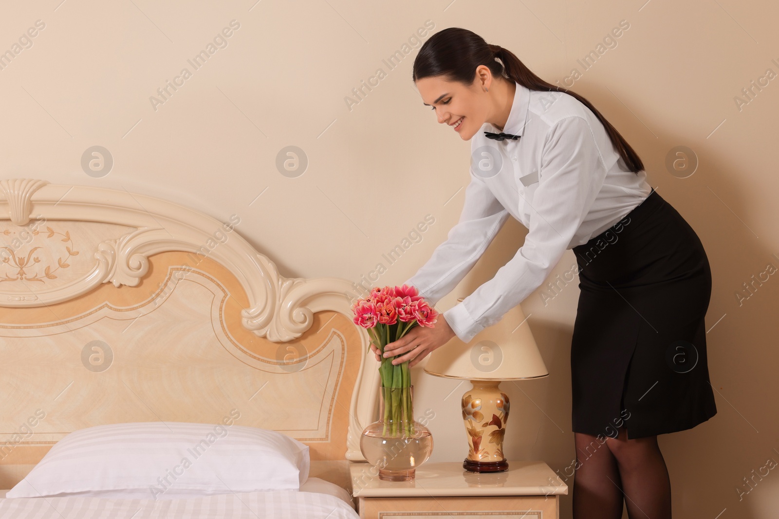 Photo of Woman putting flowers near bed in hotel room, space for text. Professional butler courses