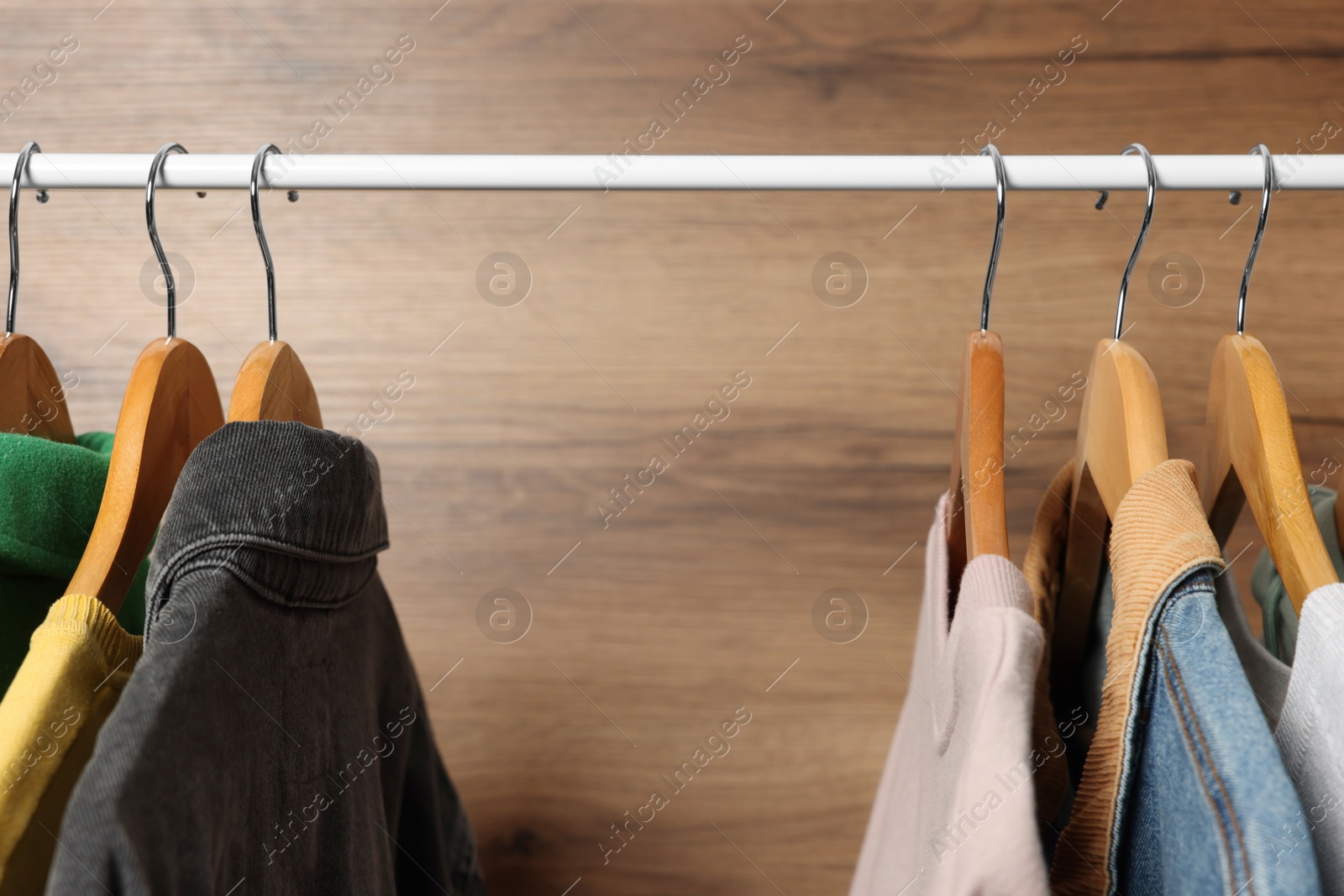 Photo of Hangers with stylish women`s clothes on rack near wooden wall, closeup