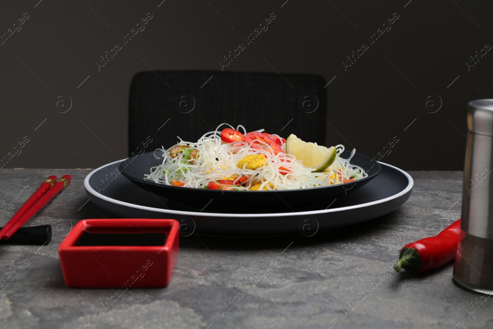 Photo of Stir-fry. Tasty rice noodles with meat and vegetables served on grey textured table