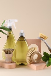 Bottles of cleaning product, brushes and floral decor on beige background