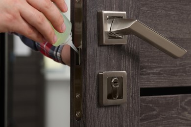 Photo of Handyman lubricating door lock with oil indoors, closeup