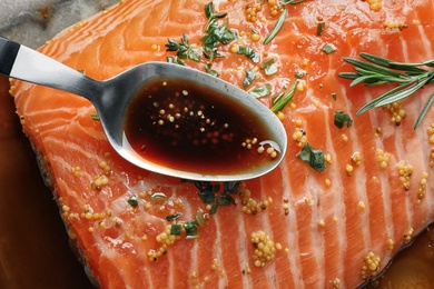 Photo of Spoon with marinade on raw salmon fillet, closeup