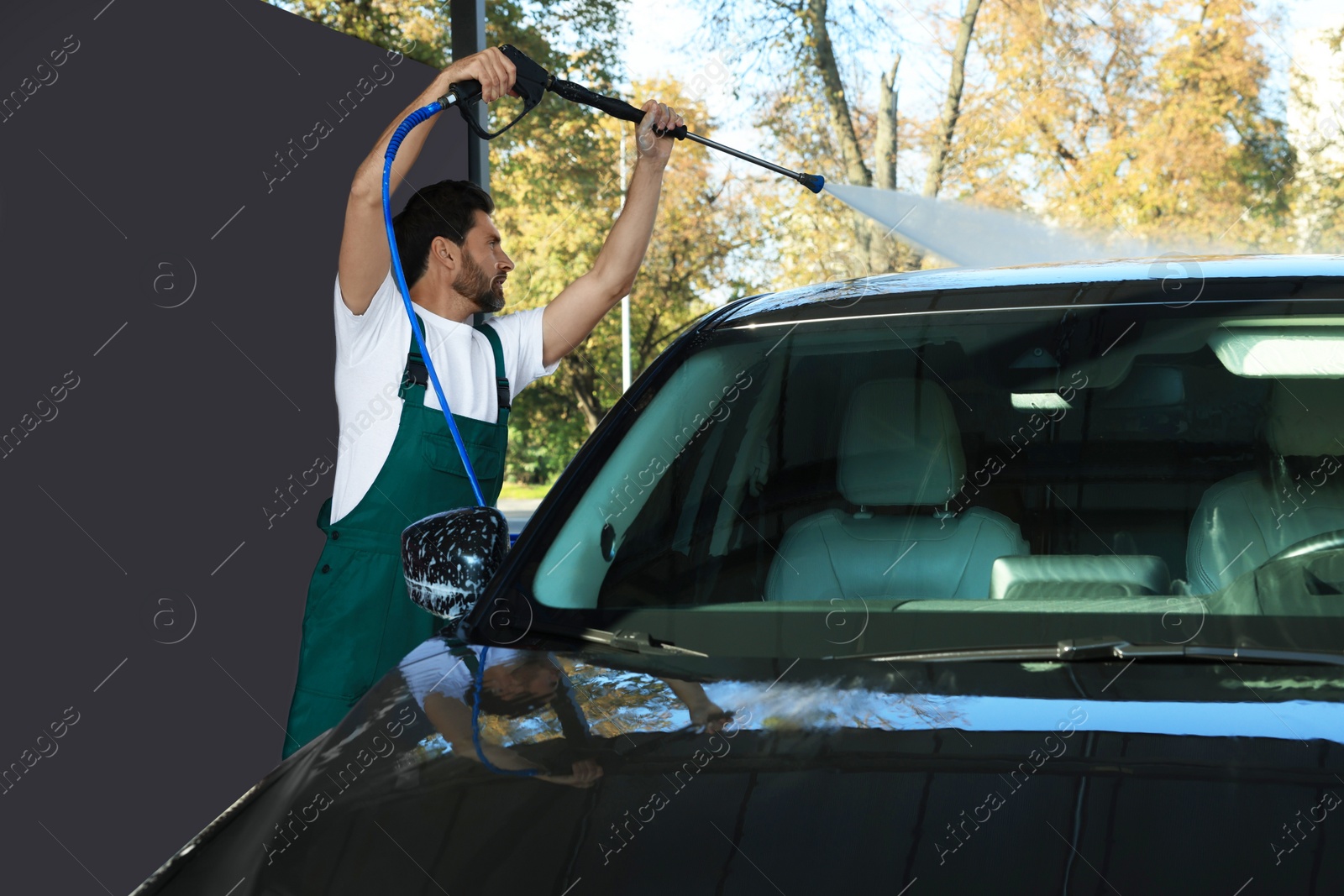 Photo of Worker washing auto with high pressure water jet at outdoor car wash