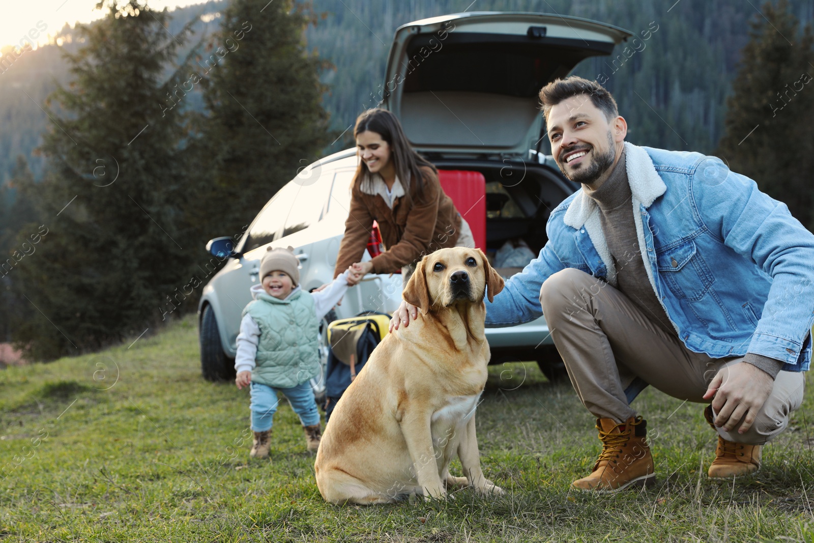 Photo of Happy man with dog, mother and her daughter near car in mountains. Family traveling with pet