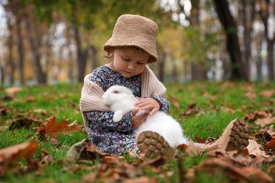 Photo of Girl hugging cute white rabbit on grass in autumn park