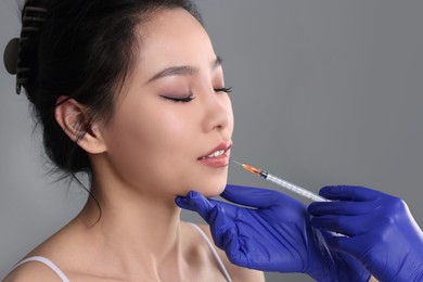 Photo of Woman getting lip injection on grey background, closeup