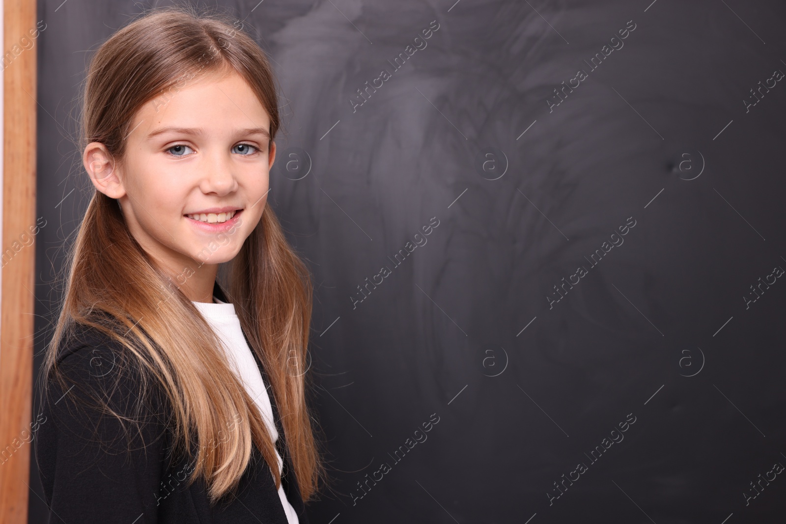 Photo of Smiling schoolgirl near blackboard. Space for text