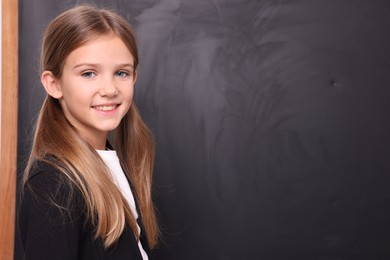 Photo of Smiling schoolgirl near blackboard. Space for text