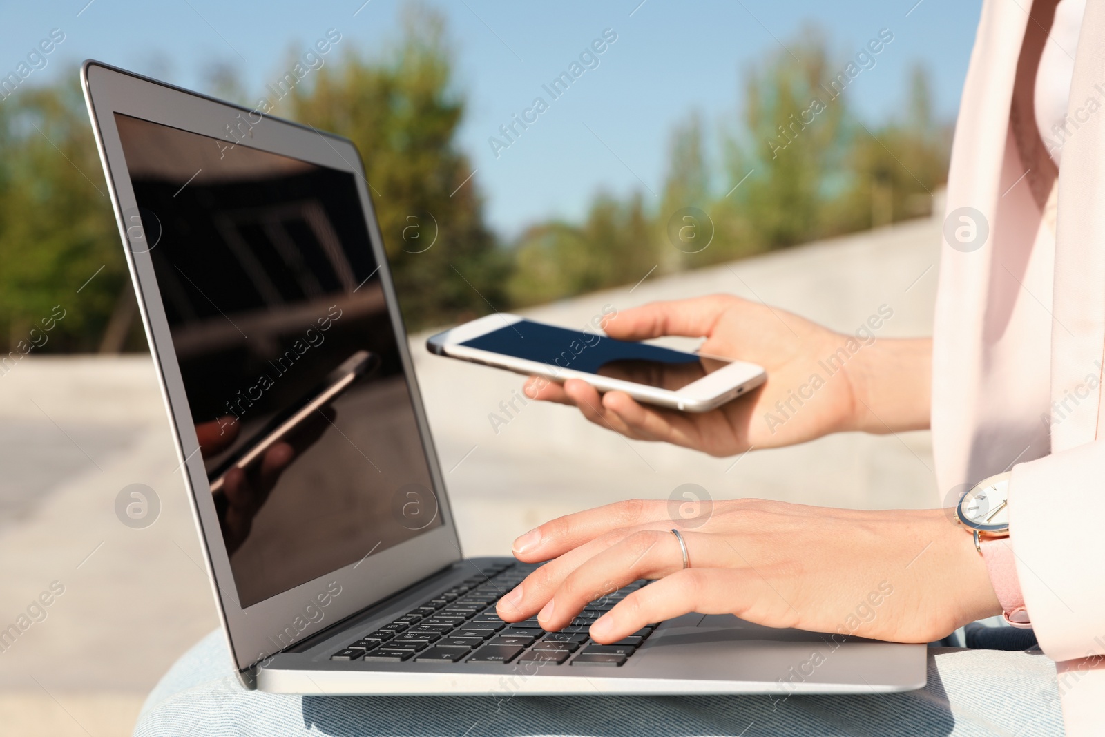 Image of Young woman using phone and laptop outdoors, closeup