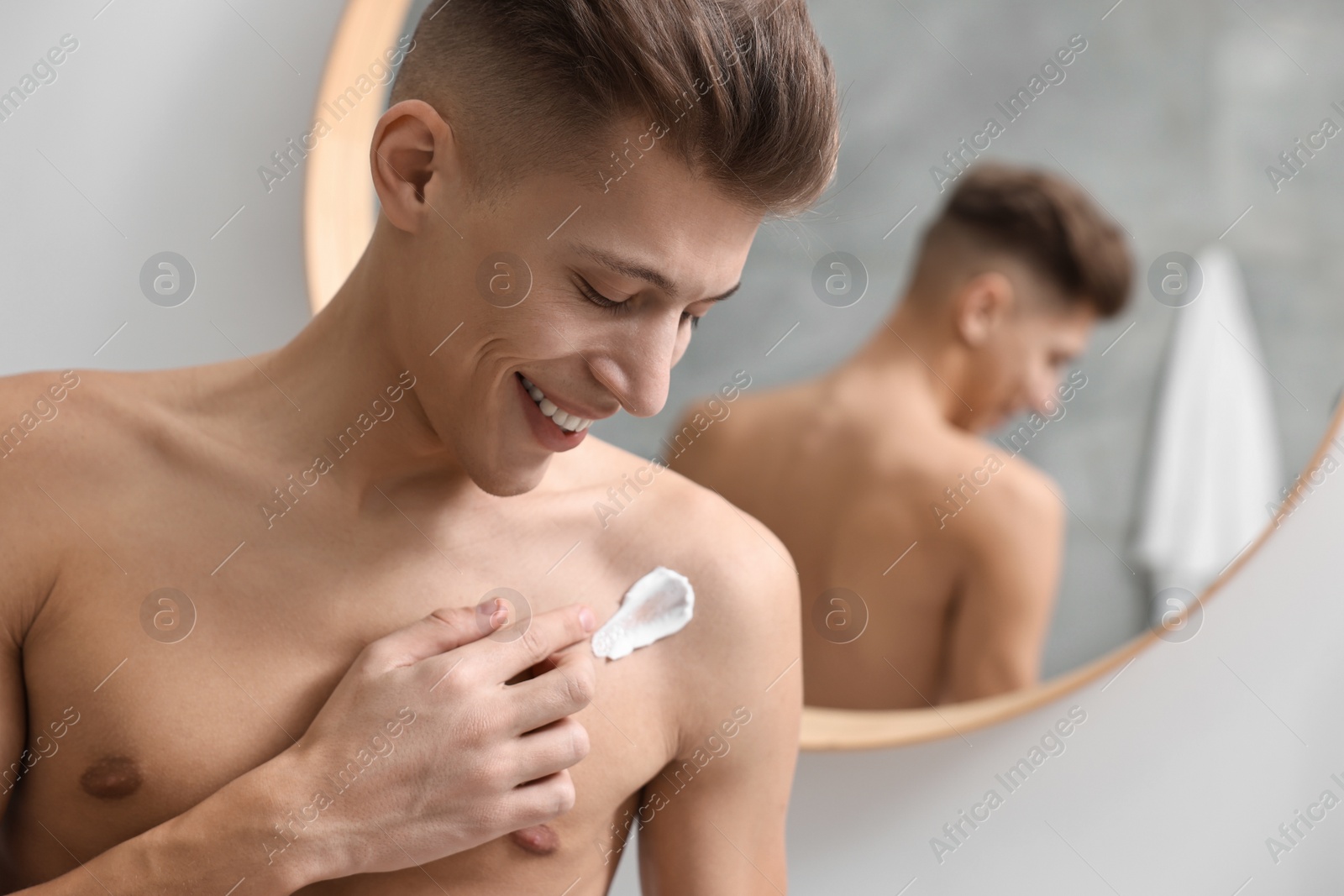 Photo of Handsome man applying moisturizing cream onto his shoulder indoors. Space for text