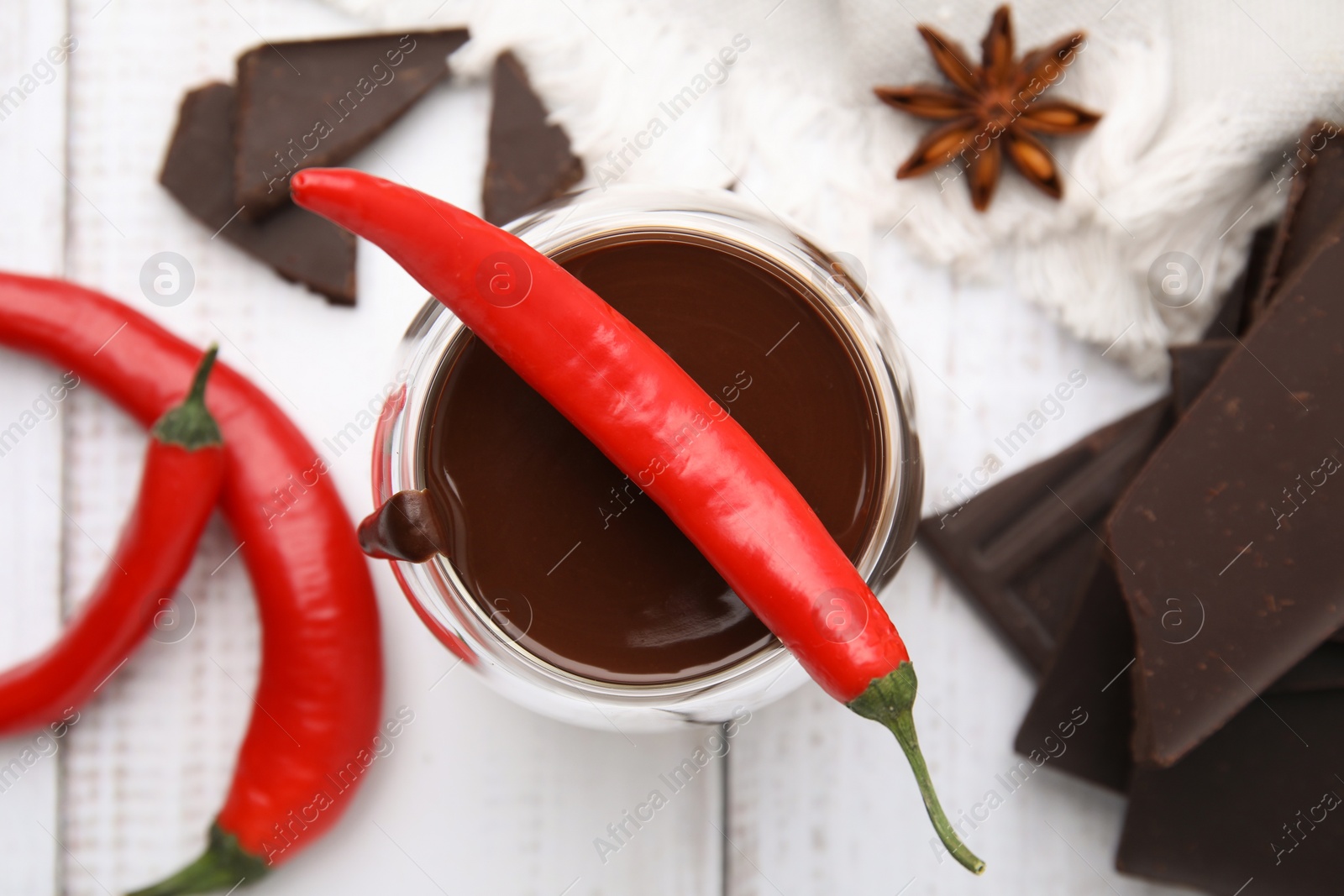 Photo of Glass of hot chocolate with chili pepper on white wooden table, flat lay