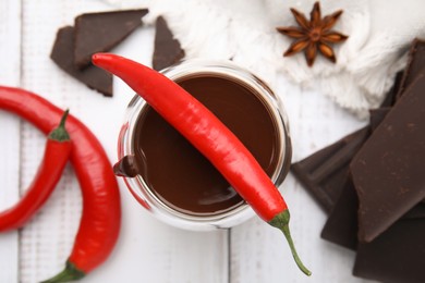 Glass of hot chocolate with chili pepper on white wooden table, flat lay