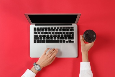 Photo of Woman with cup of coffee using modern laptop, top view