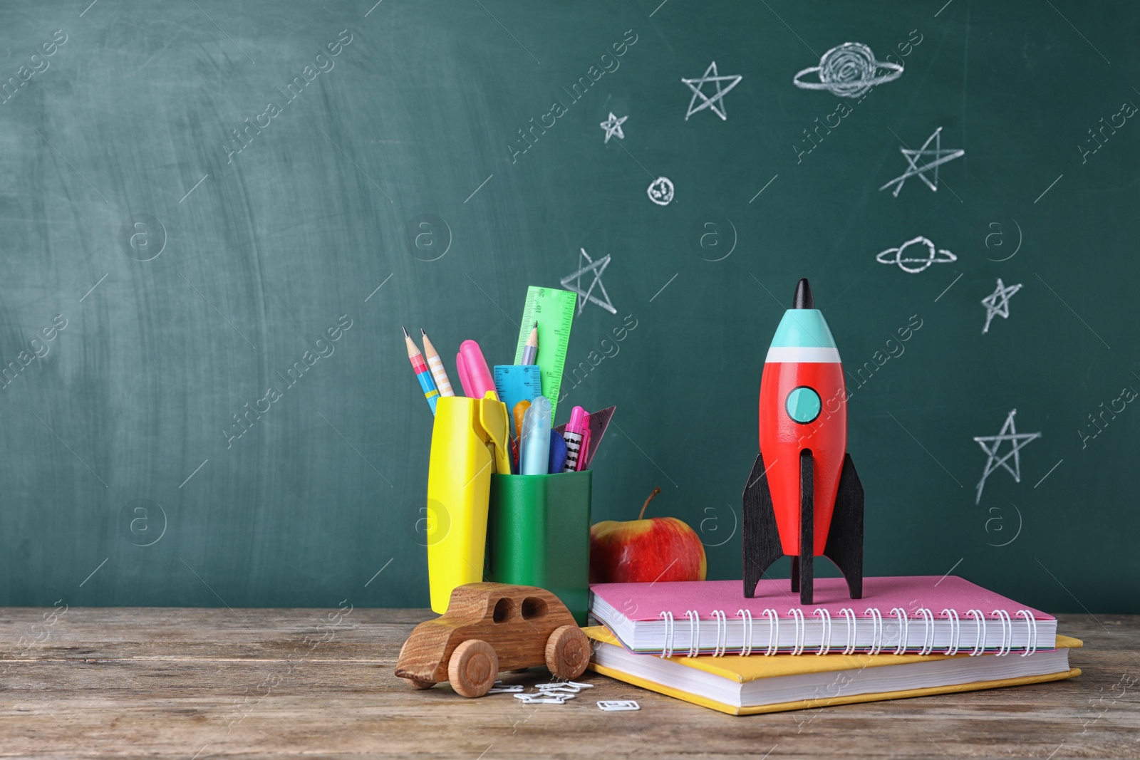 Photo of Bright toy rocket and school supplies on wooden desk. Space for text