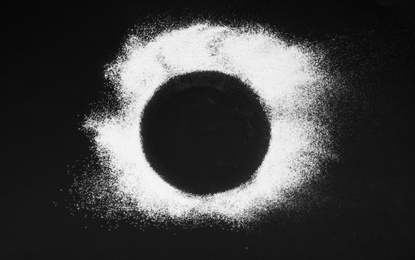 Photo of Round frame made of flour on black table, top view. Space for text