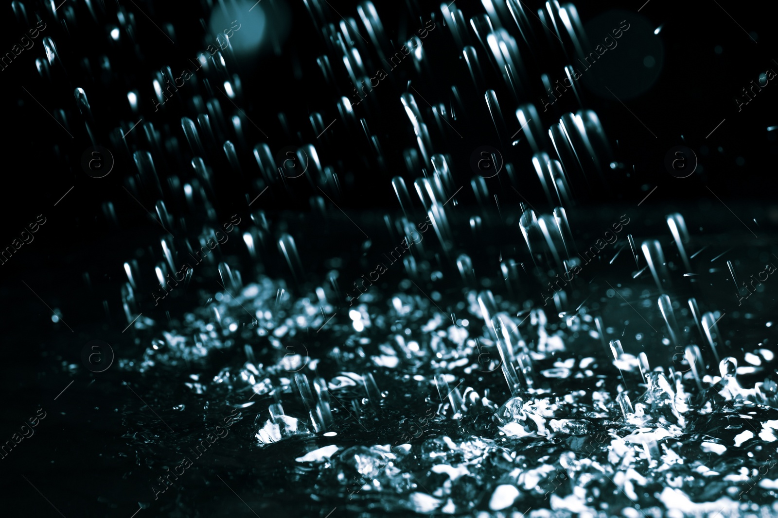 Photo of Heavy rain falling down on ground against dark background, closeup