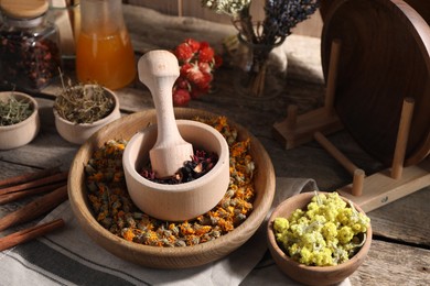 Mortar with pestle, many different dry herbs, flowers and cinnamon sticks on wooden table