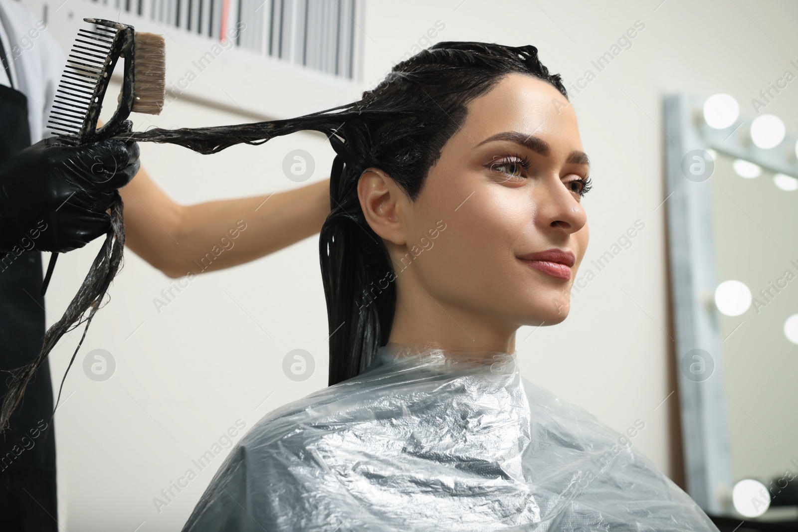 Photo of Professional hairdresser dyeing client's hair in beauty salon