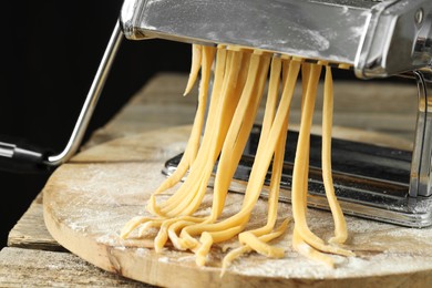 Pasta maker with raw dough on wooden table