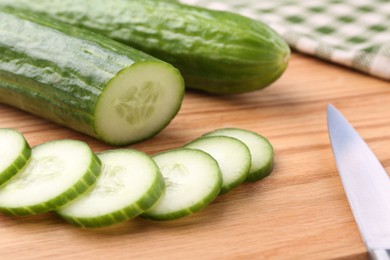 Fresh cucumbers and knife on wooden cutting board, closeup