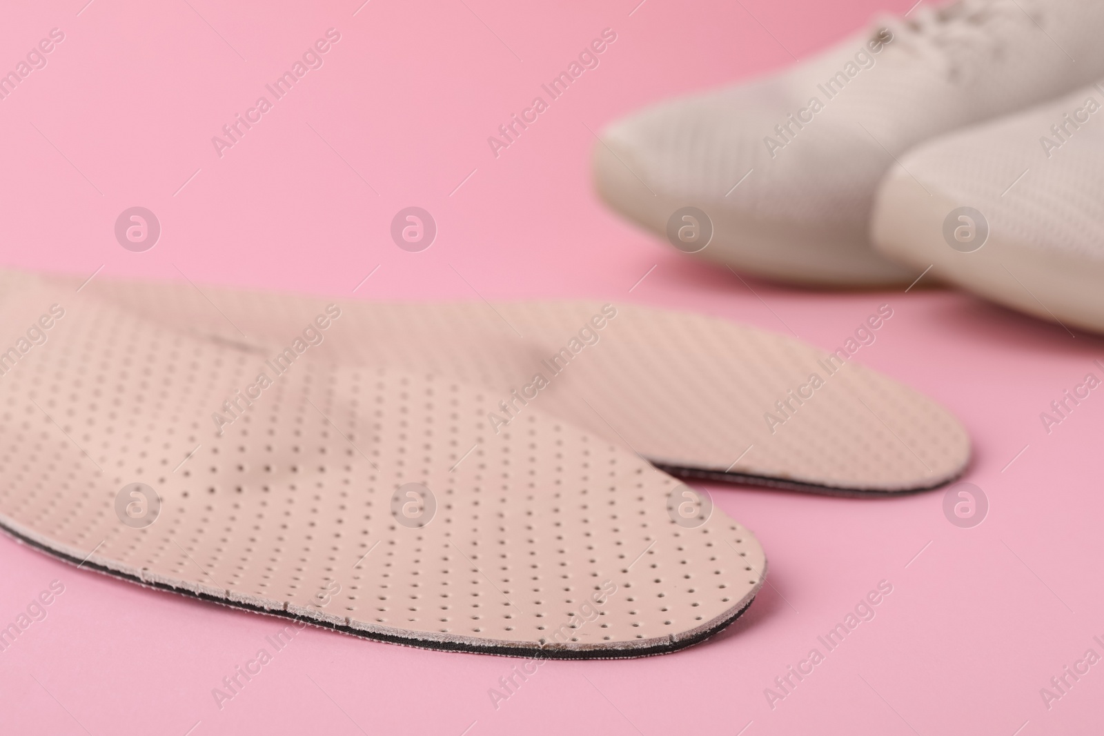 Photo of Orthopedic insoles and shoes on pink background, closeup