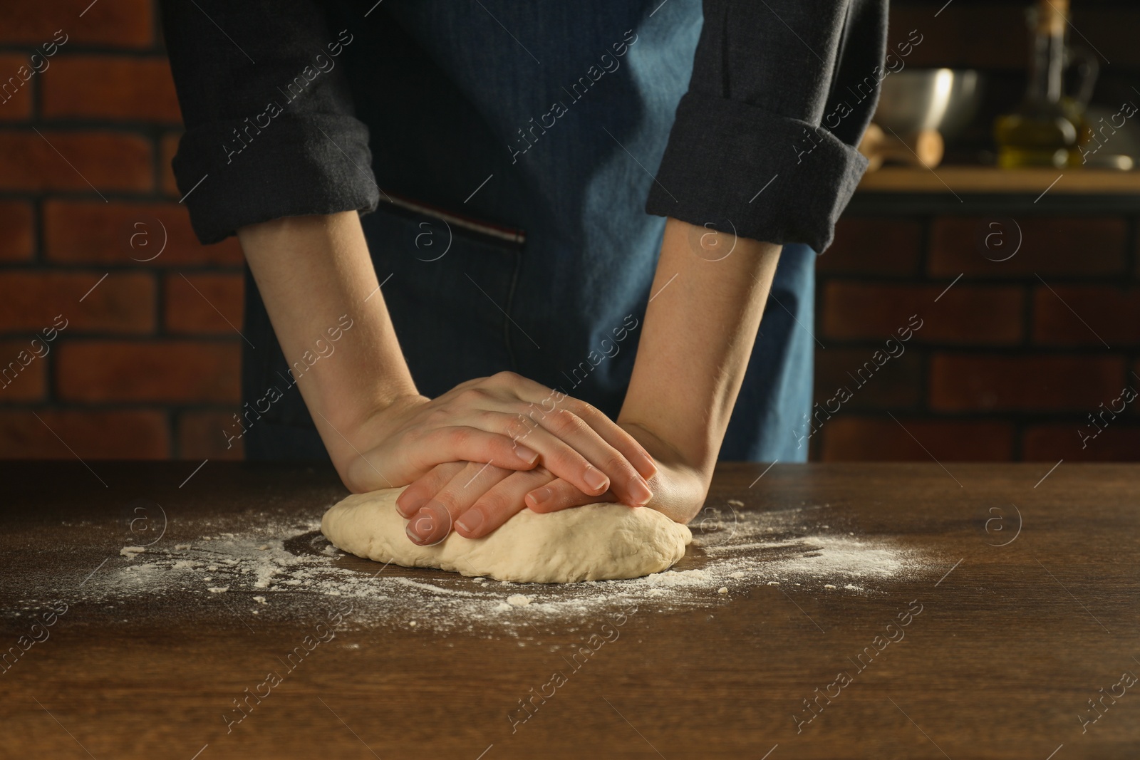 Photo of Making bread. Woman kneading dough at wooden table in kitchen, closeup