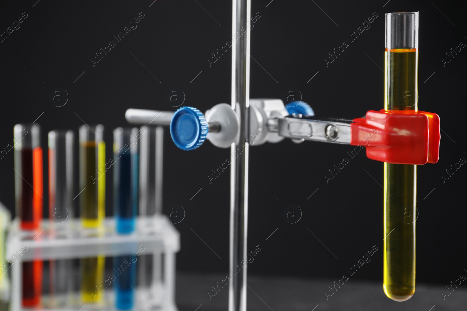 Photo of Retort stand and test tube with liquid on black background, closeup