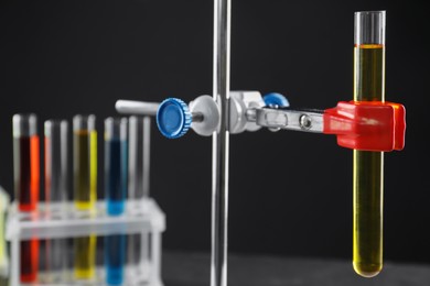 Photo of Retort stand and test tube with liquid on black background, closeup