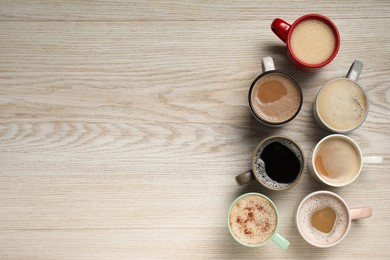 Photo of Many cups with different aromatic coffee on light wooden table, flat lay. Space for text