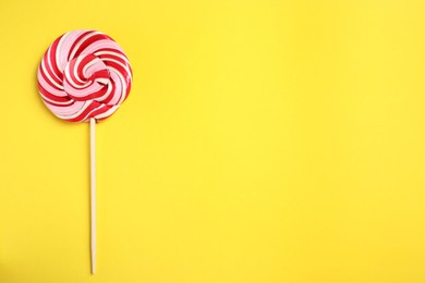 Stick with colorful lollipop swirl on yellow background, top view. Space for text