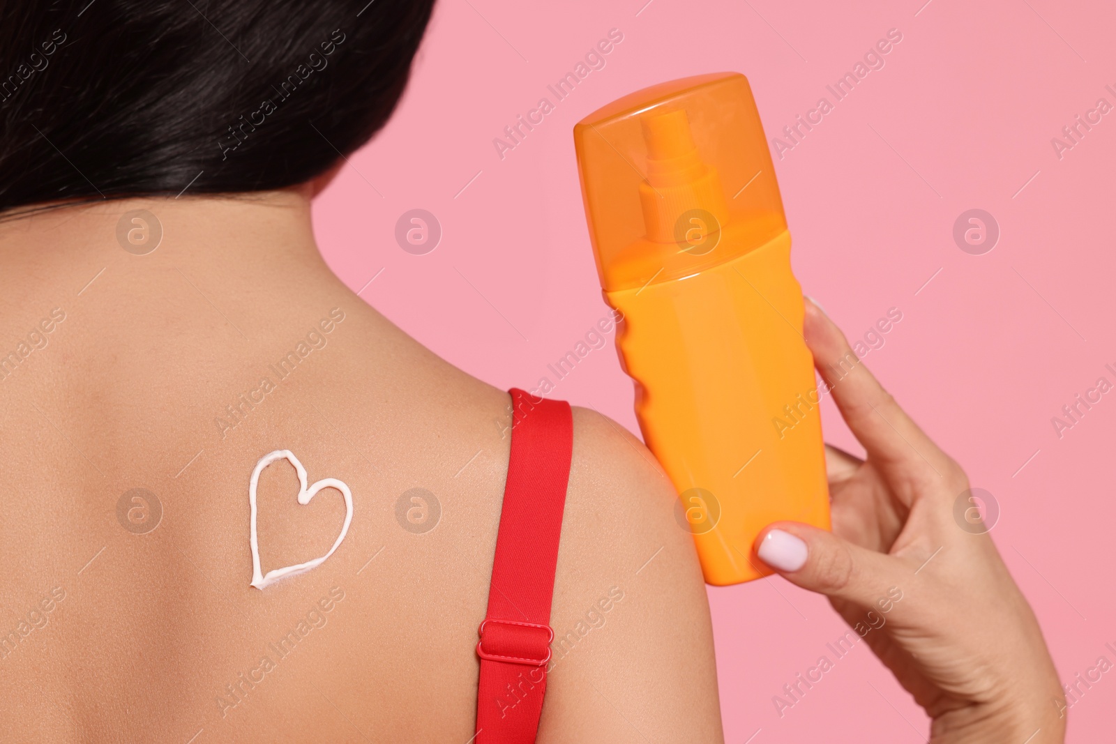 Photo of Young woman with sun protection cream on her back against pink background, closeup