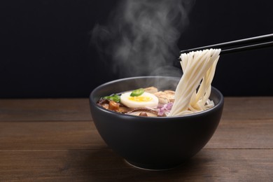 Image of Eating hot vegetarian ramen with chopsticks at wooden table against black background. Space for text