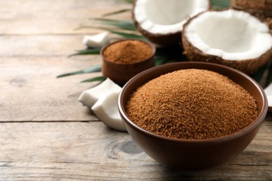 Photo of Natural coconut sugar in bowl on wooden table, space for text