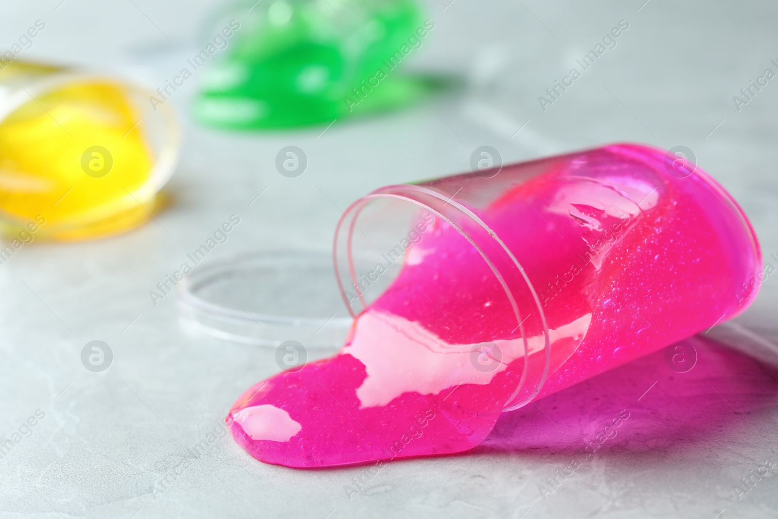 Photo of Overturned plastic container with pink slime on marble background, closeup