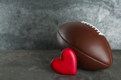 American football ball and heart on grey table. Space for text