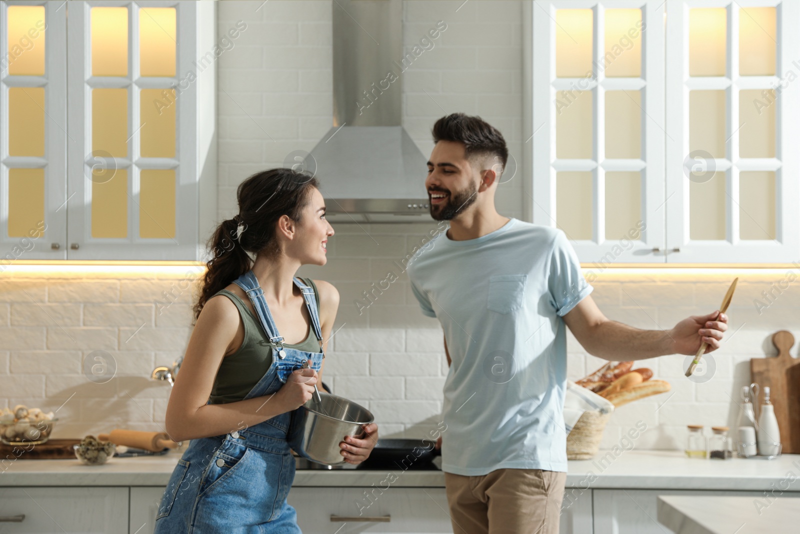 Photo of Lovely young couple dancing while cooking together in kitchen