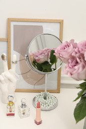 Photo of Mirror, cosmetic products, perfumes and vase with pink roses on white dressing table