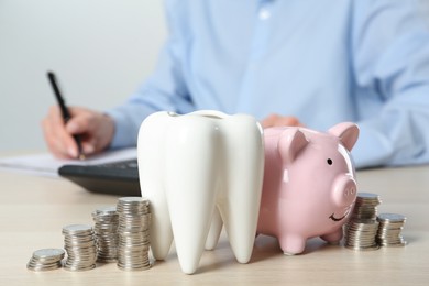 Photo of Ceramic model of tooth, piggy bank and coins on wooden table. Expensive treatment