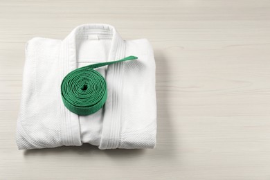 Photo of Green karate belt and white kimono on wooden background, top view. Space for text