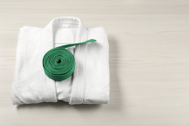 Green karate belt and white kimono on wooden background, top view. Space for text