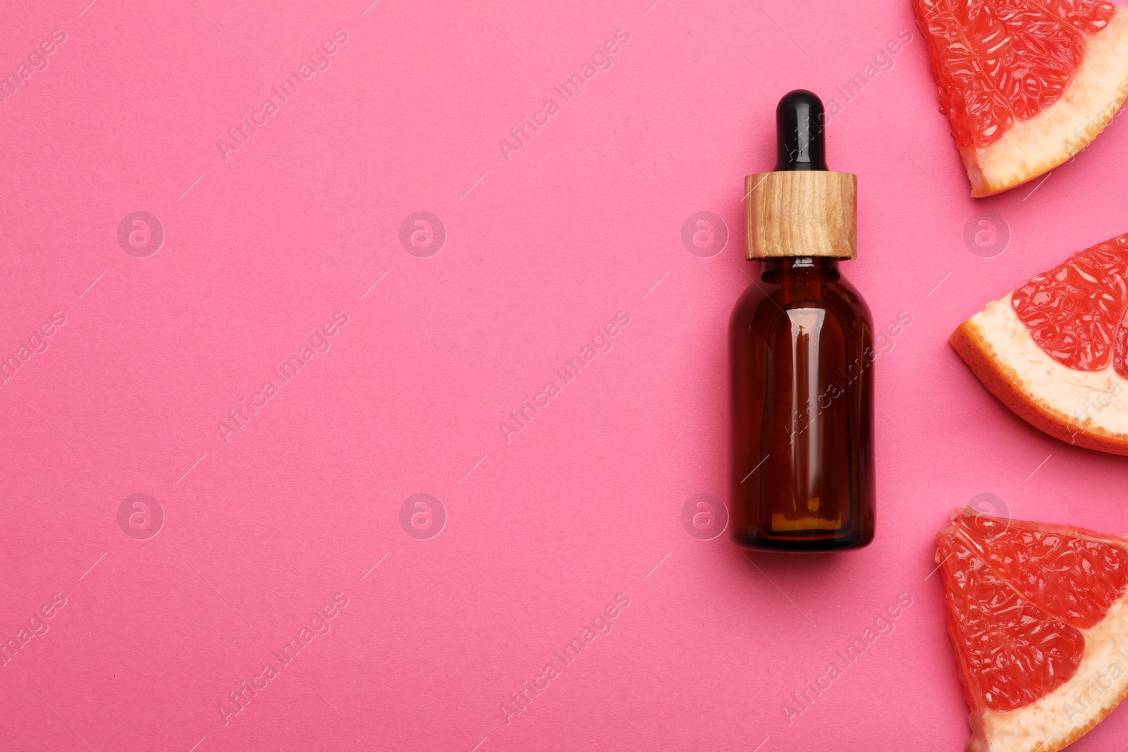 Photo of Bottle of citrus essential oil and fresh grapefruit slices on pink background, flat lay. Space for text