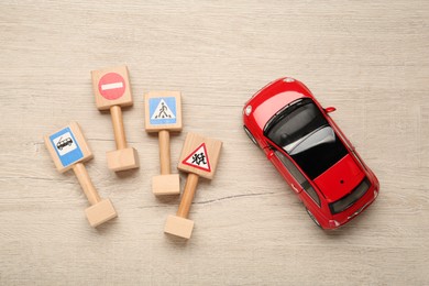 Photo of Different miniature road signs and car on wooden table, flat lay. Driving school