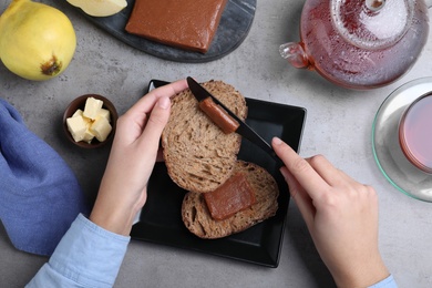 Photo of Woman spreading delicious quince paste on toast bread at grey table, top view