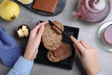 Woman spreading delicious quince paste on toast bread at grey table, top view