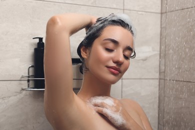 Photo of Beautiful woman washing hair with shampoo in shower
