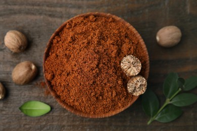 Photo of Nutmeg powder in bowl, seeds and green leaves on wooden table, flat lay