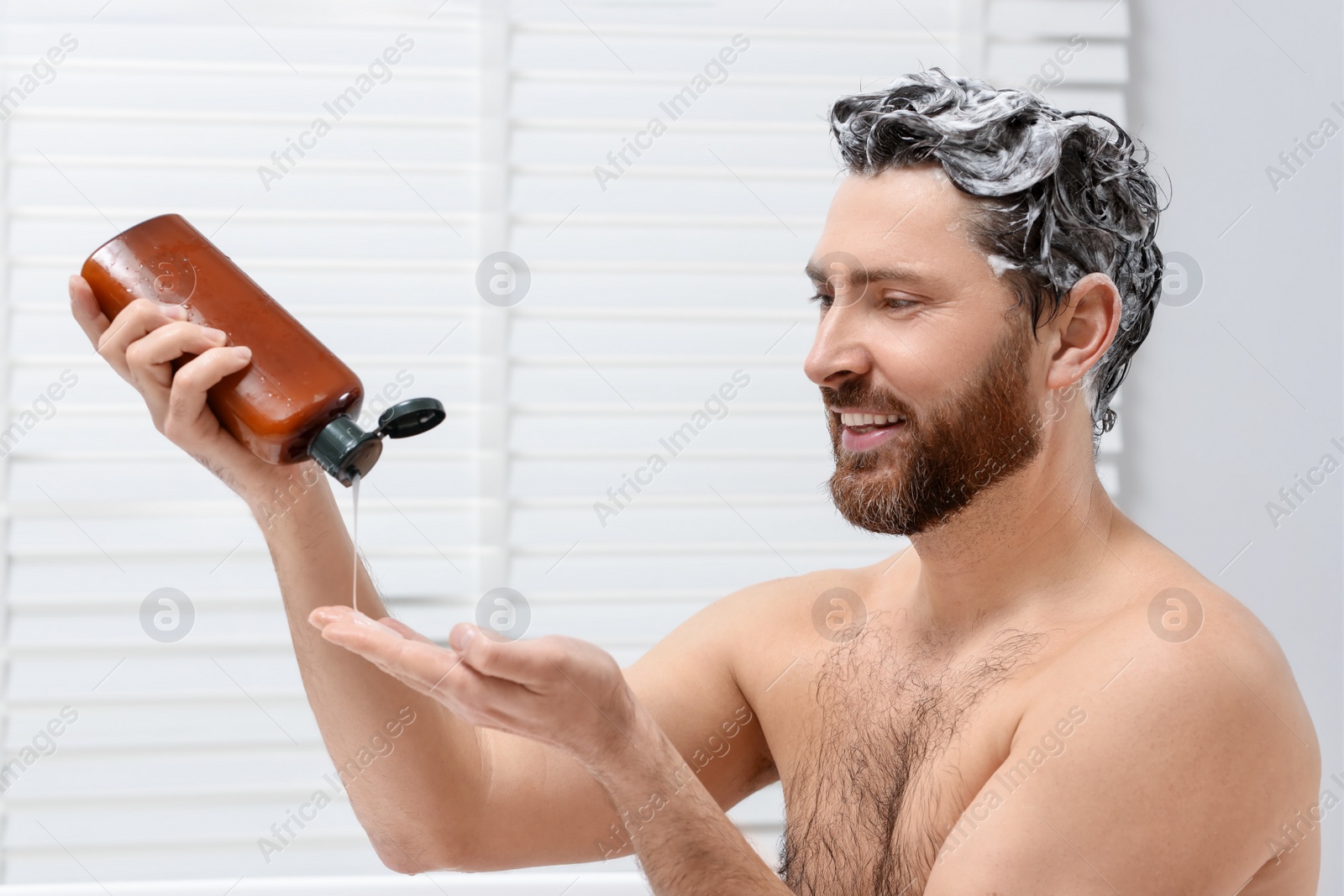 Photo of Happy man pouring shampoo onto his hand in shower