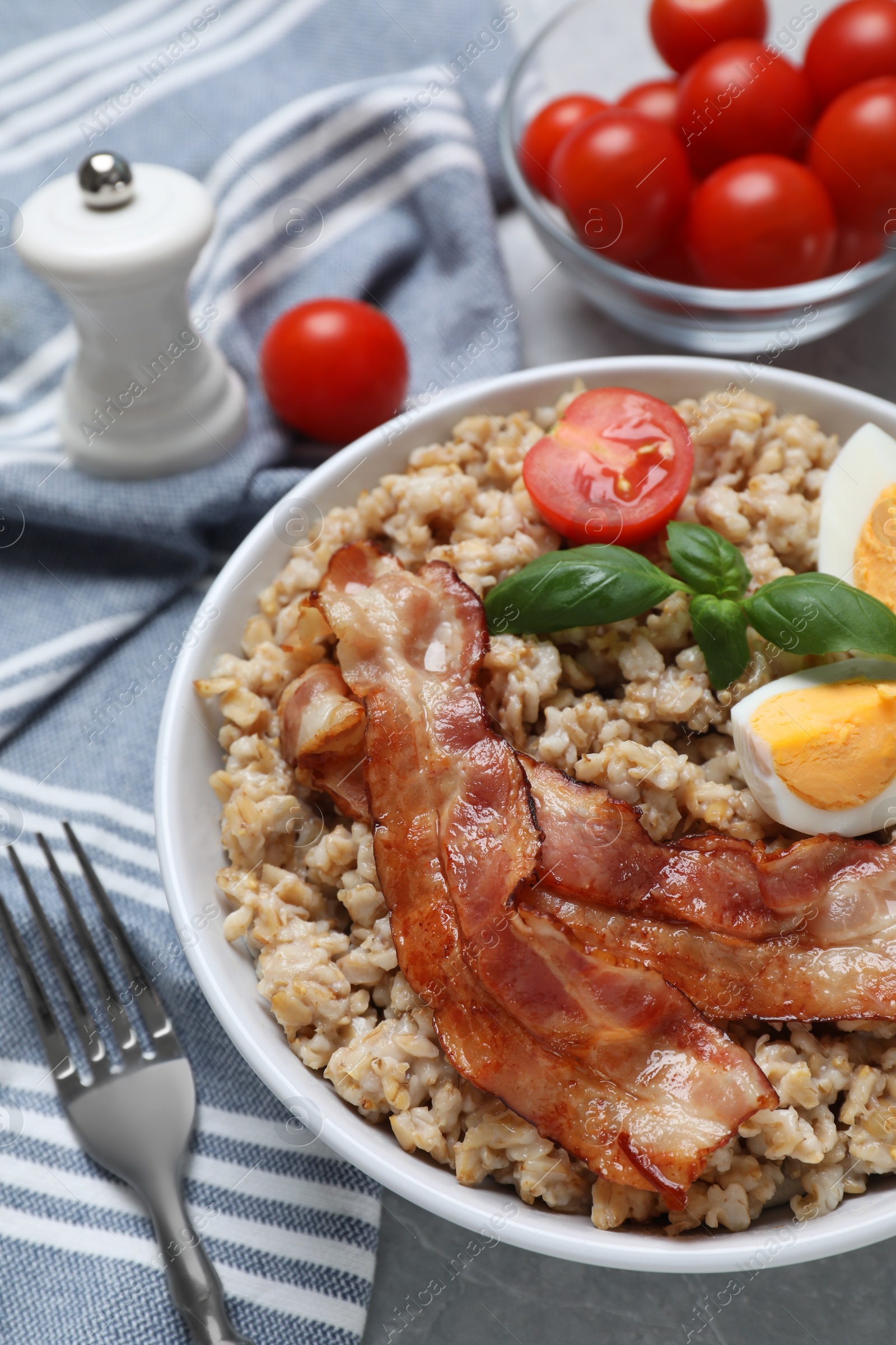 Photo of Tasty boiled oatmeal with egg, bacon and tomatoes served on light grey table, closeup