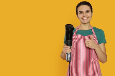 Photo of Beautiful young woman holding sous vide cooker on orange background. Space for text