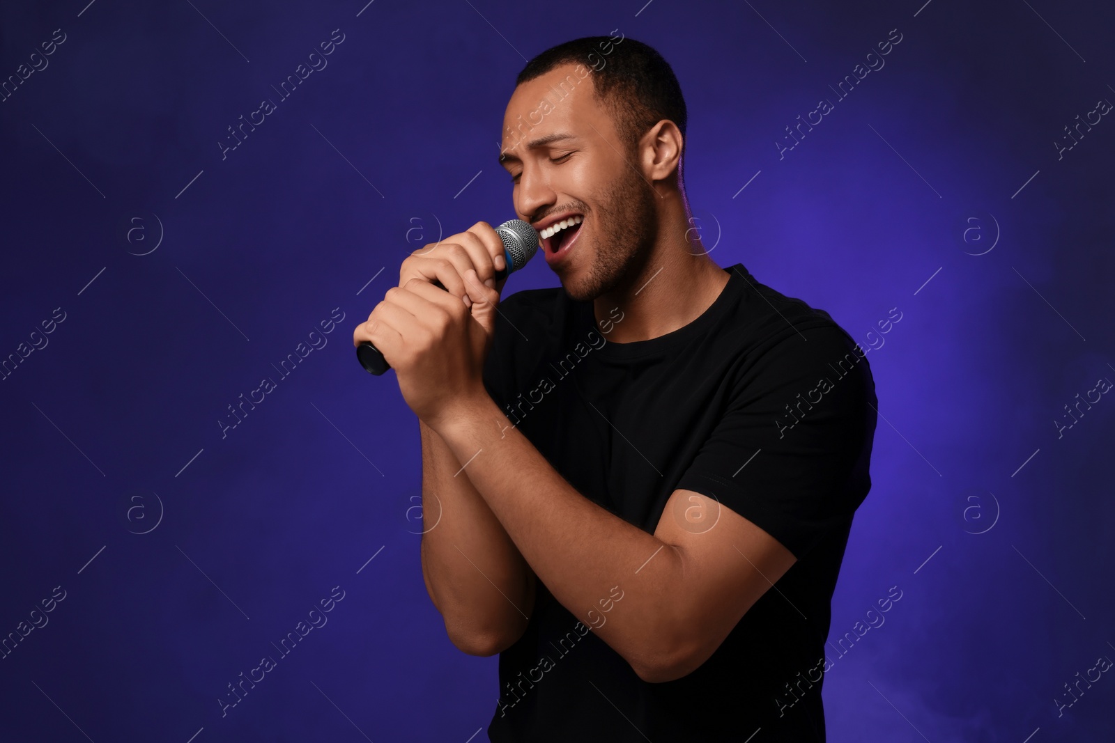 Photo of Handsome man with microphone singing on blue background